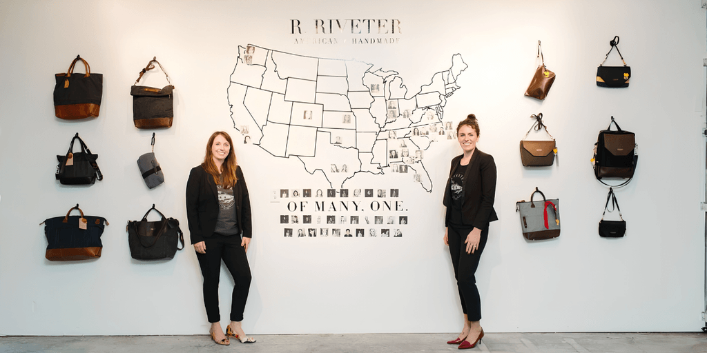 Two women stand in front of a wall displaying bags and a map of the USA
