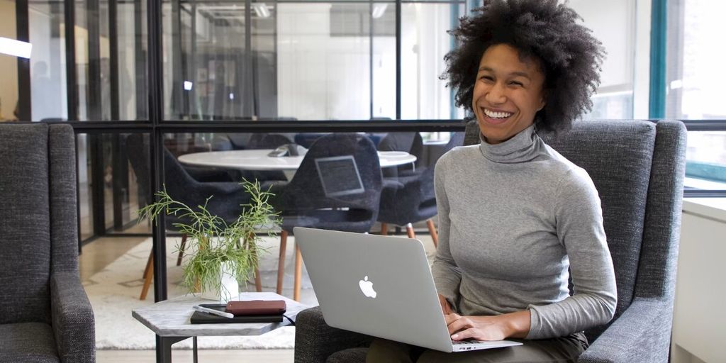 Smiling businesswoman working on laptop in modern office, representing female leadership and career success.