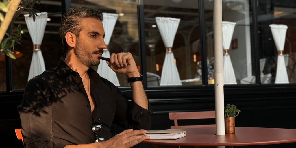 "Johnny Abraham, relationship mentor and author, reflects thoughtfully at an outdoor café, embodying his teachings of emotional growth."