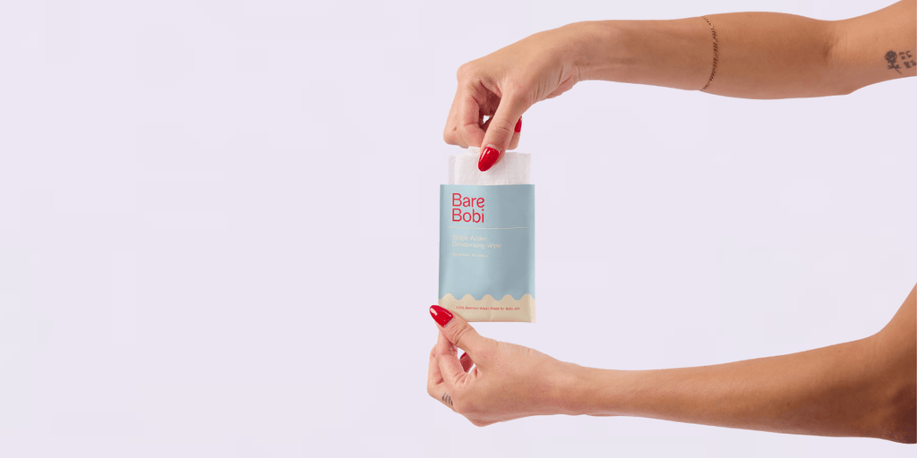 Hand pulling Bare Bobi deodorising wipe from packet against clean background.