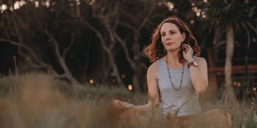 Lea Clothier sitting outdoors in meditation with hands resting on her knees.