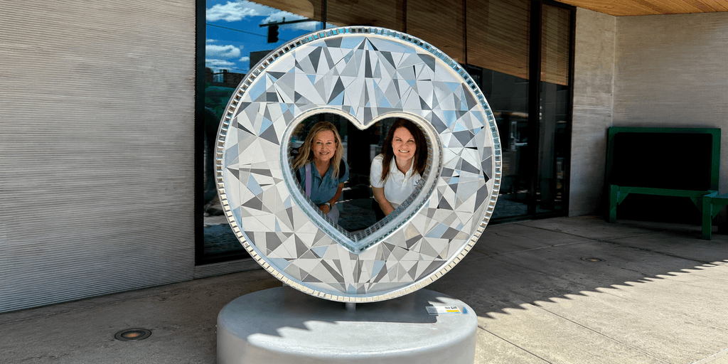 Danielle Marten and Tami Wood pose inside a heart-shaped public art sculpture representing family connection.