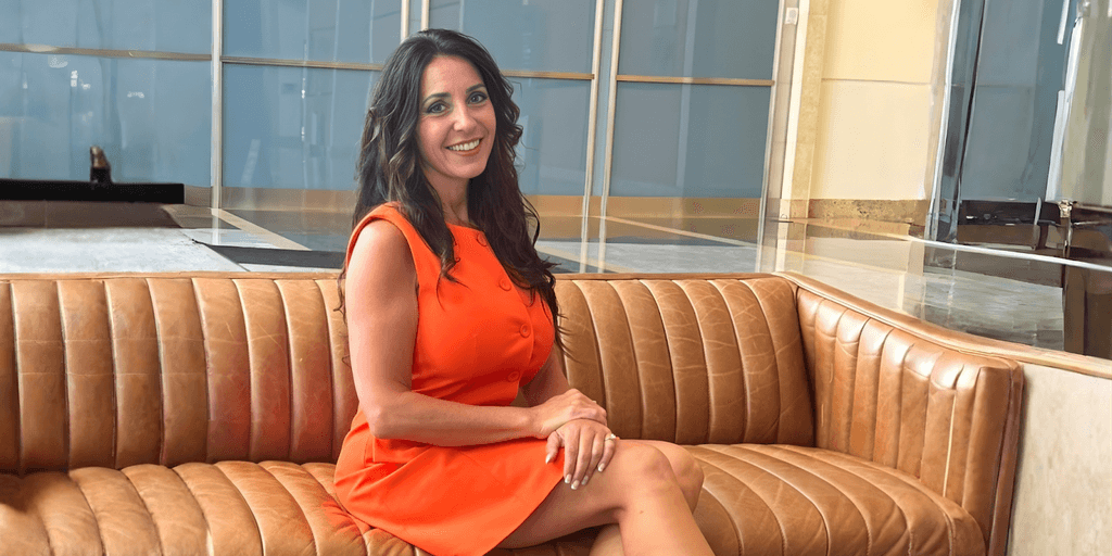 Dr. Cathy Sarvis smiling in a bright orange dress on a couch.