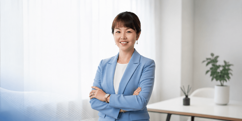 Professional woman in a light blue blazer standing confidently with arms crossed in a modern office.