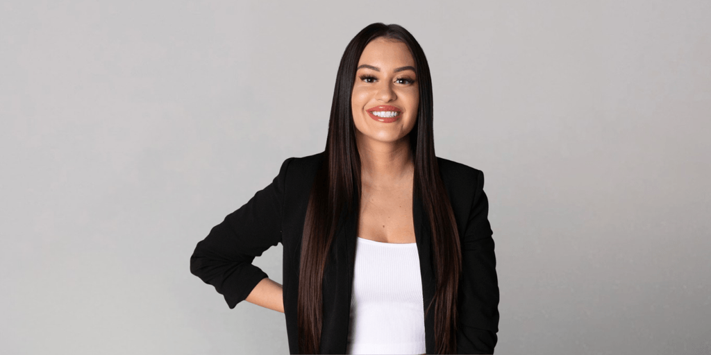 Erica Battista smiling in a black blazer against a neutral gray background.