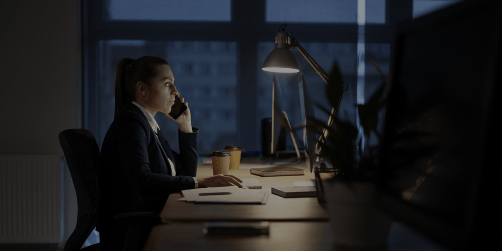 Business professional working late at a desk while talking on the phone in an office.