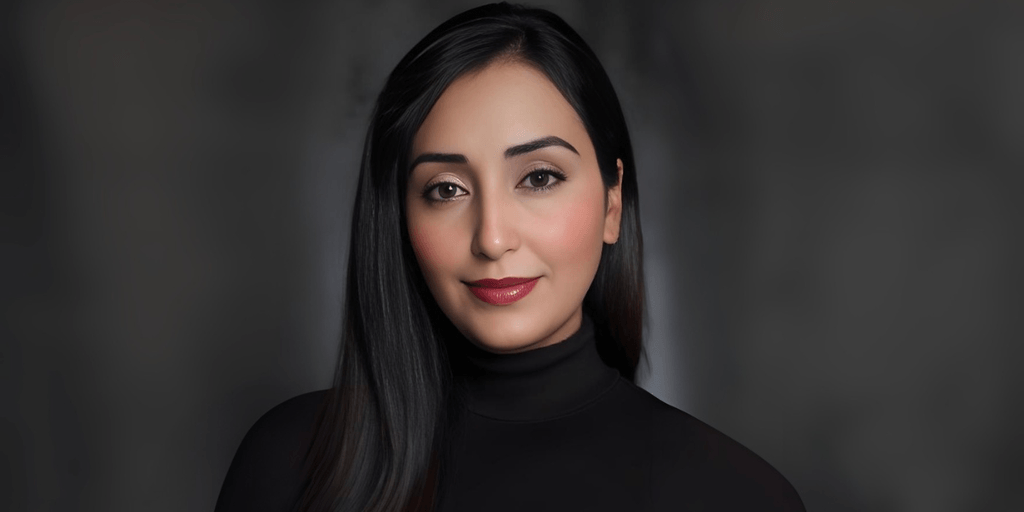 "Portrait of a woman with long black hair and neutral makeup, wearing a black turtleneck top, exuding a professional and confident look against a blurred background."