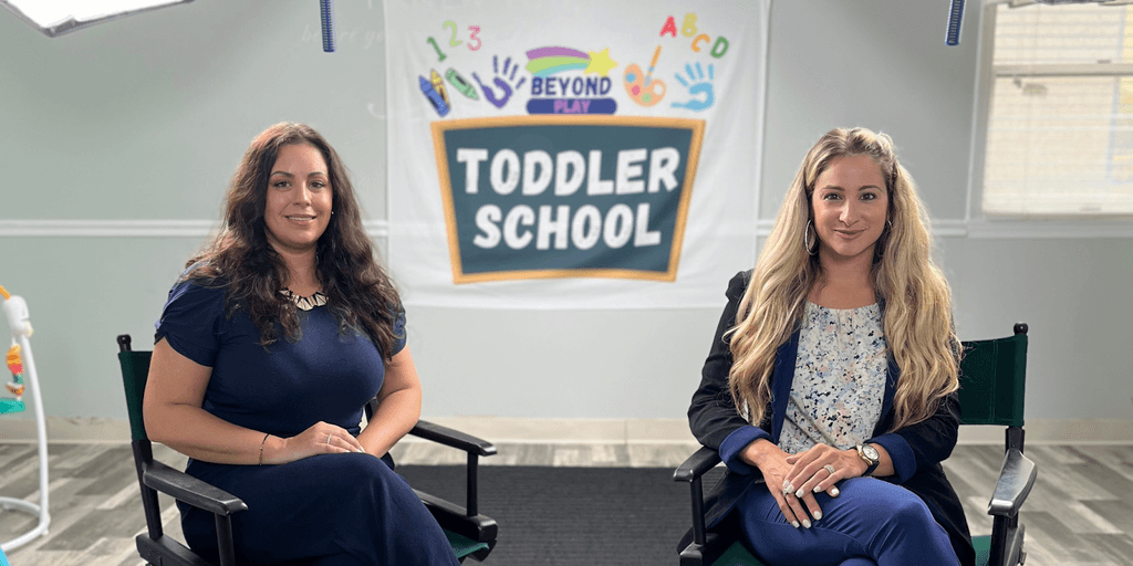 Two women sit in front of a “Toddler School” banner at Beyond Play NYC learning center.