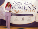 A woman in purple attire stands beside a banner for a women's business bazaar