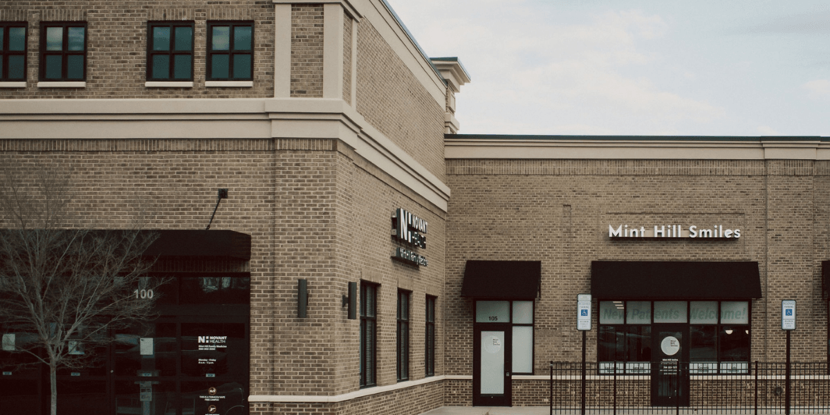 Brick building exterior featuring two storefronts with signs for Mint Hill Smiles and wellness services