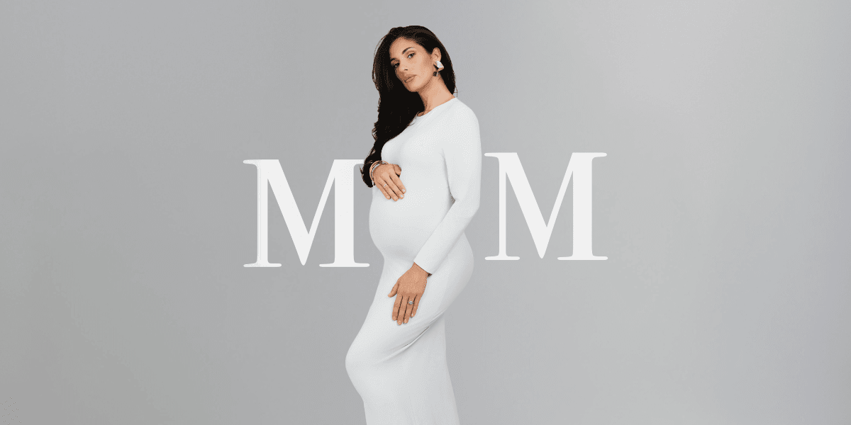 Pregnant woman in a white dress poses stylishly against a neutral background
