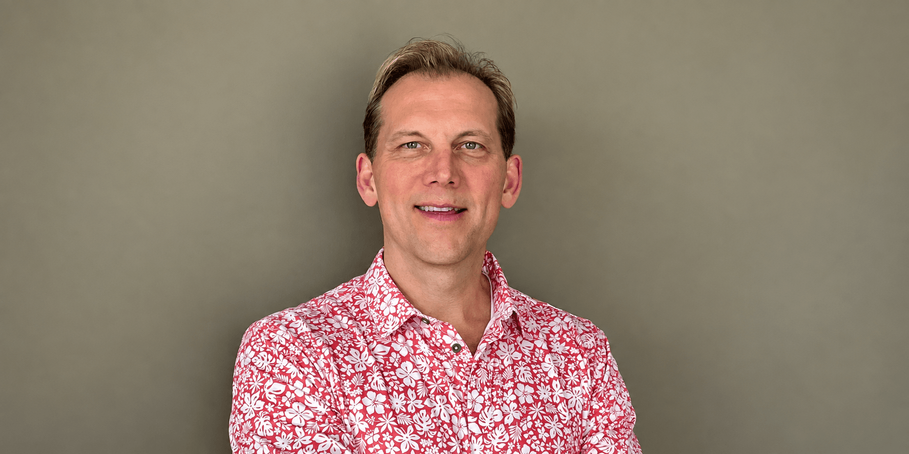 Smiling man in a floral shirt posing with arms crossed against a neutral background