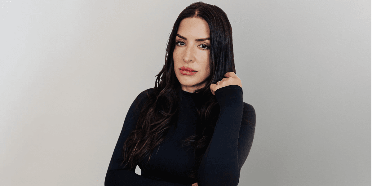 Woman with long dark hair wearing a black fitted top poses against a neutral background