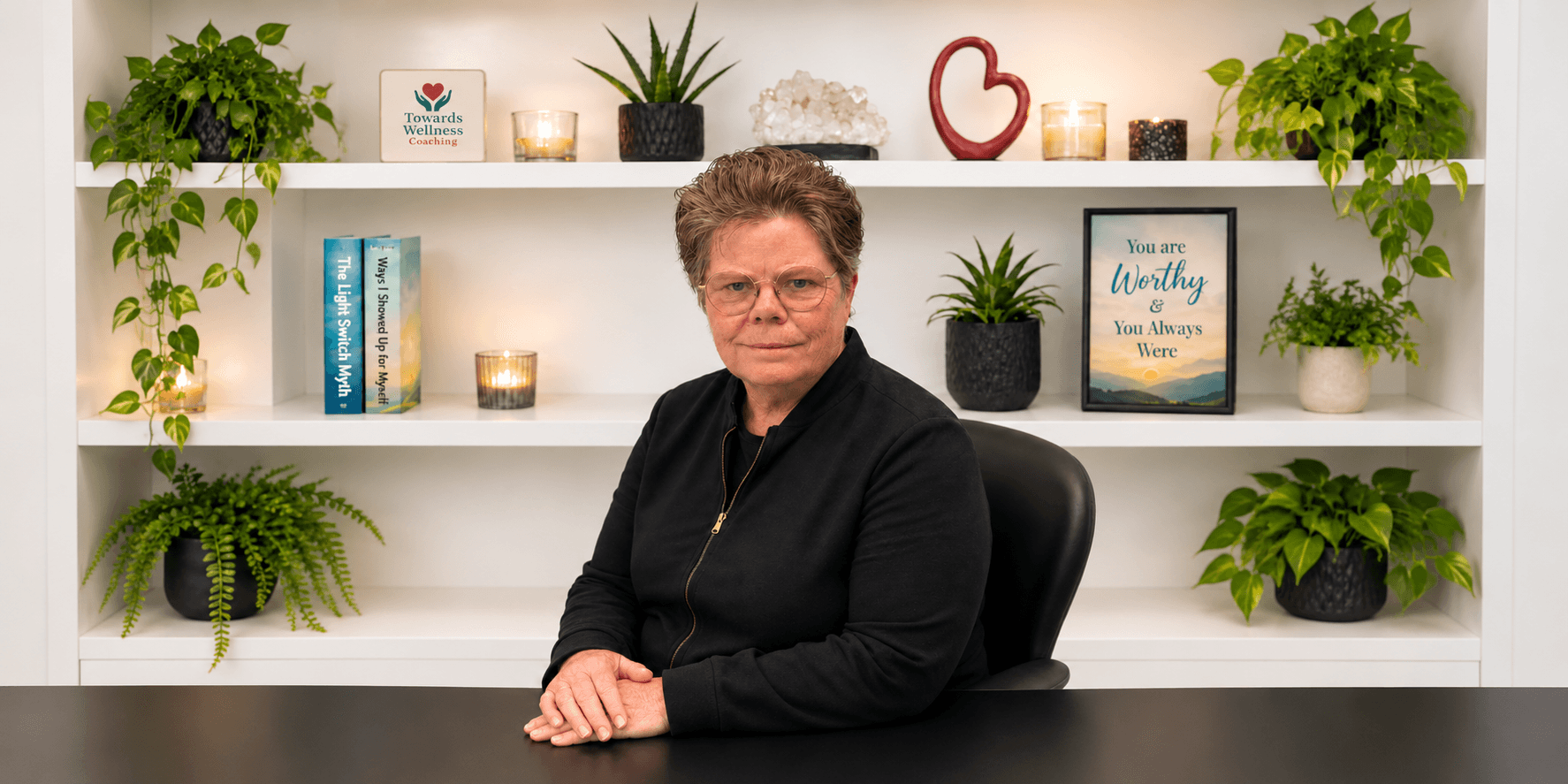 A woman sits at a desk in front of a well-decorated shelf with plants.