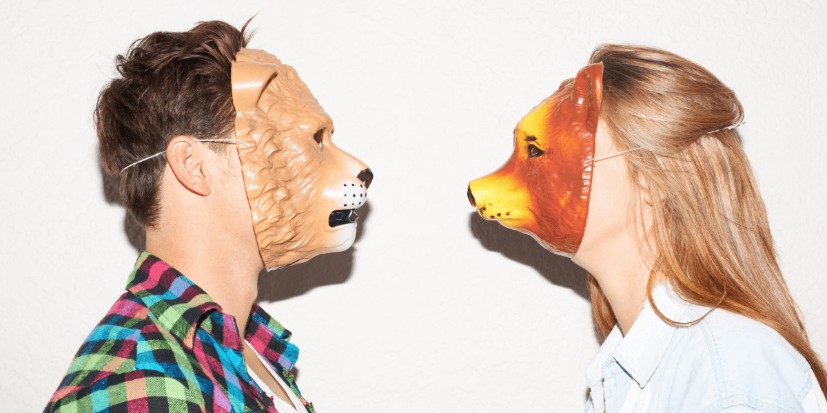 Two people wearing animal masks face each other against a plain background