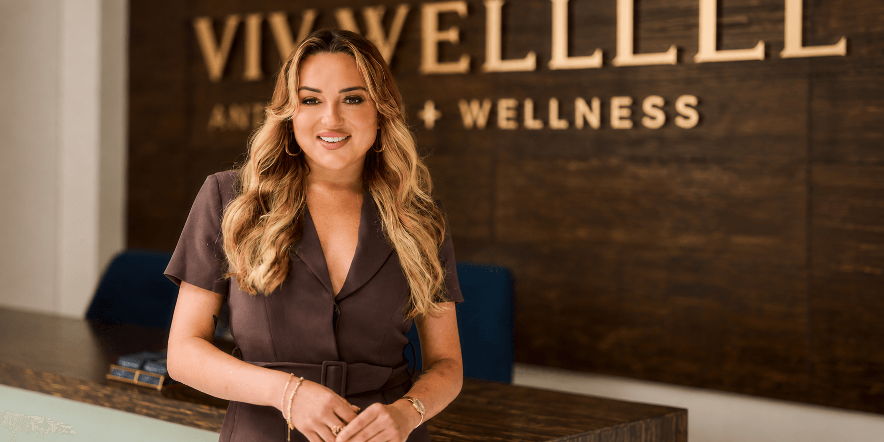 A smiling woman stands at a reception desk in a wellness center