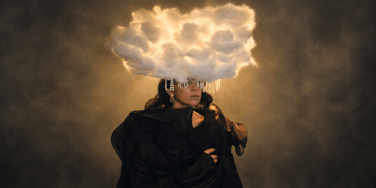 A figure with a cloud-shaped headpiece adorned with crystals against a dramatic background