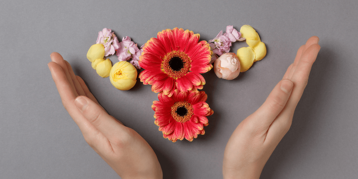 Two hands holding vibrant flowers arranged in a heart shape on a gray background