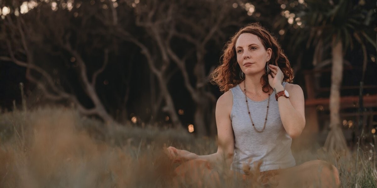 Lea Clothier sitting outdoors in meditation with hands resting on her knees.