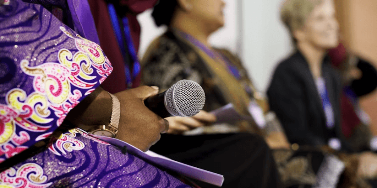 Woman holding a microphone during a panel discussion at a professional women's business event.