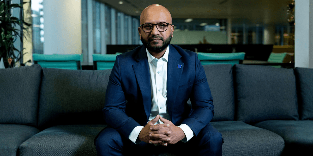 Business professional in a blue suit seated on a sofa in a modern office.