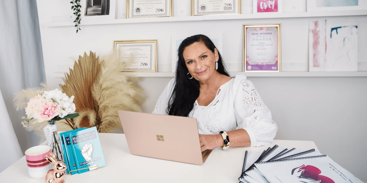 Woman sitting at a desk with awards and notebooks in a bright office setting