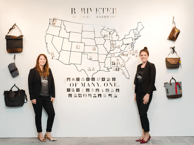 Two women stand in front of a wall displaying bags and a map of the USA
