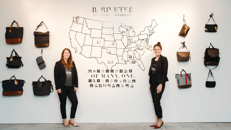 Two women stand in front of a wall displaying bags and a map of the USA