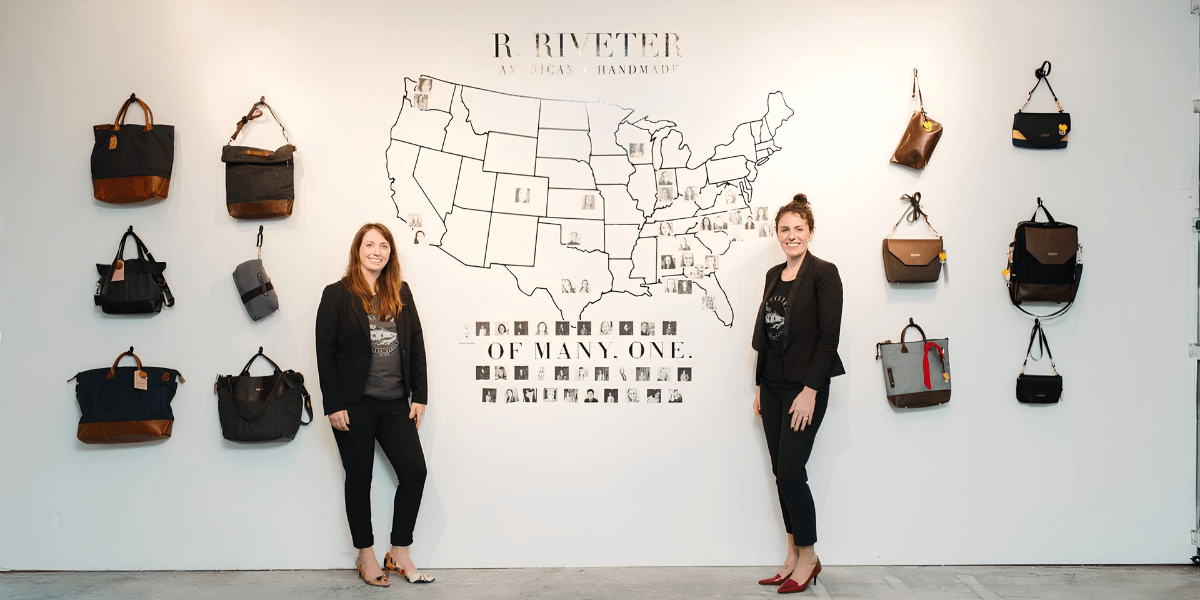 Two women stand in front of a wall displaying bags and a map of the USA