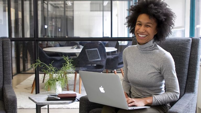 Smiling businesswoman working on laptop in modern office, representing female leadership and career success.