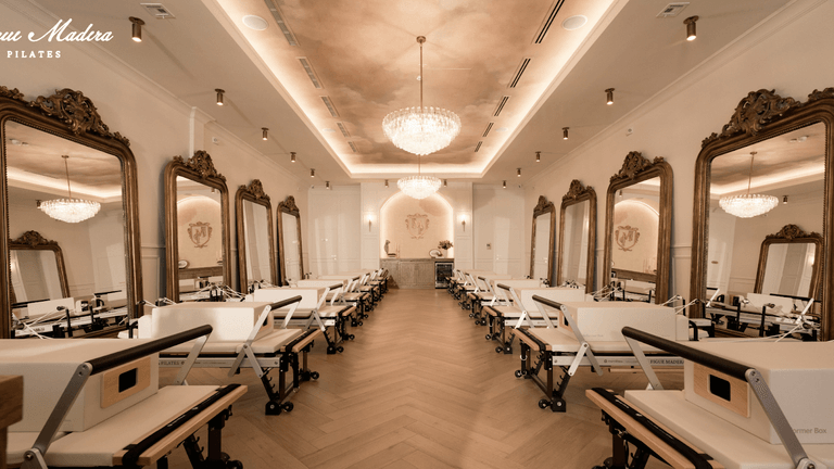 Elegant Pilates studio with reformers, chandeliers, and large mirrors for a serene atmosphere.