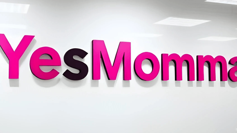 "The 'YesMomma' logo displayed in bold pink and purple letters on a white wall, showcasing a modern and vibrant design."
