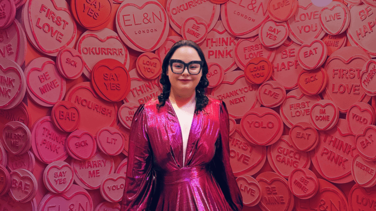 Woman in pink dress stands before heart-themed wall at EL&N London, representing healing and empowerment from heartbreak.