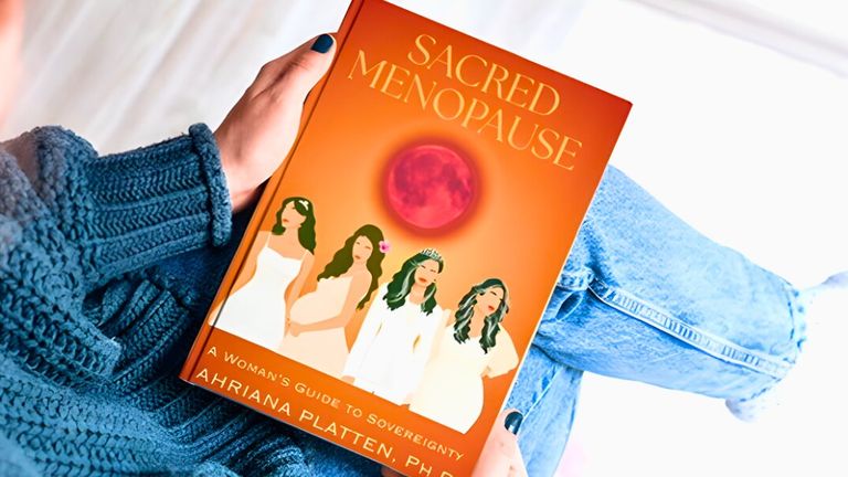 A person holding the book Sacred Menopause by Dr. Ahriana Platten, featuring a colorful cover and empowering message.