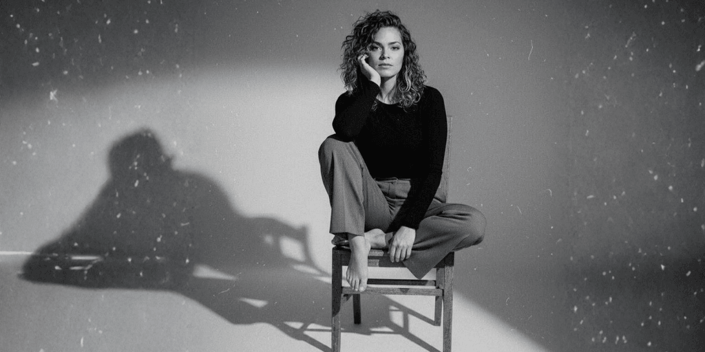 Black-and-white portrait of woman sitting on chair, dramatic lighting casting shadow, contemplative expression.