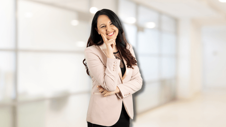 Samya Ilaria Di Donato, a confident woman in a pink blazer, smiles thoughtfully with one hand on her chin.