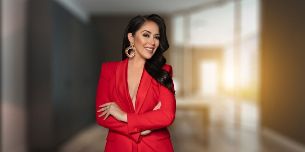 A confident woman in a red blazer smiles with her arms crossed, embodying elegance and leadership in the fashion industry.
