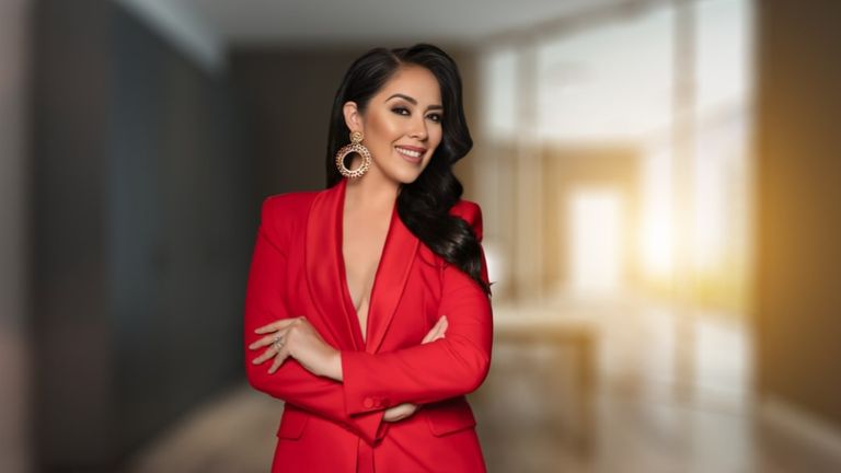 A confident woman in a red blazer smiles with her arms crossed, embodying elegance and leadership in the fashion industry.