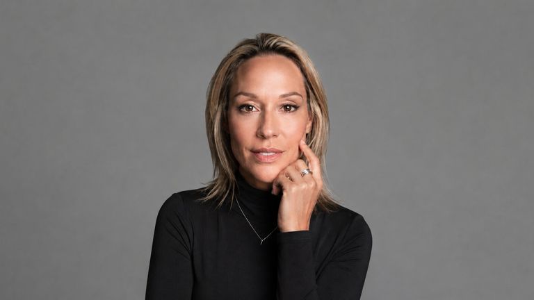 Coach Julianne wearing a black turtleneck in a professional studio portrait against a gray background.