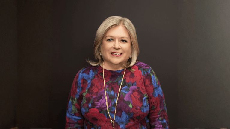 Marcy Westcott, meditation teacher and author, smiling in a colorful floral sweater against a dark background.