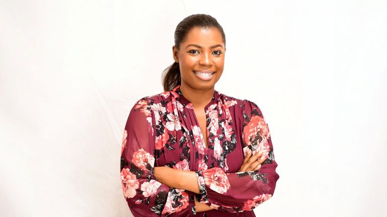 Abigail Owusu smiling with arms crossed in floral dress against white studio background.