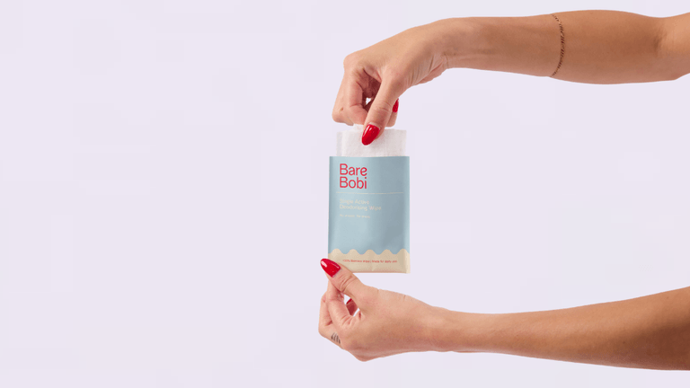 Hand pulling Bare Bobi deodorising wipe from packet against clean background.