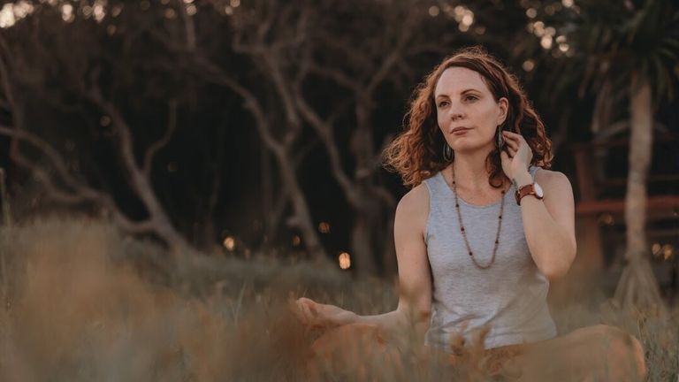 Lea Clothier sitting outdoors in meditation with hands resting on her knees.