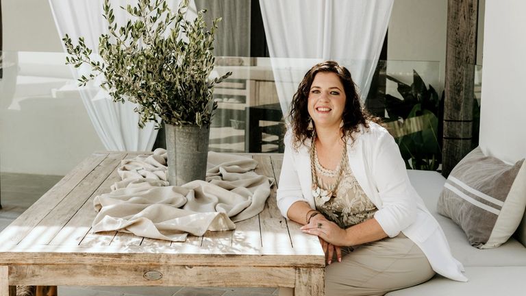 Vanessa Grace sitting at a table with a relaxed, welcoming smile, surrounded by natural decor.