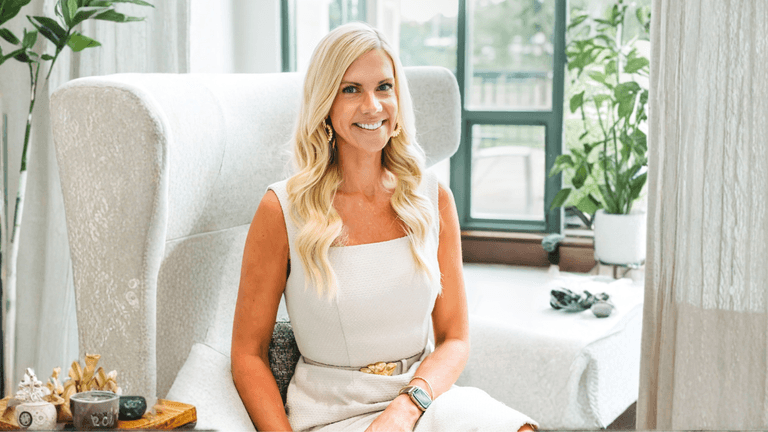 Sara Lewis Hartley smiling while seated in a calming, light-filled space promoting emotional wellness.