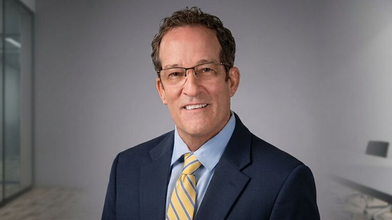 Professional headshot of financial advisor in navy suit and yellow striped tie in modern office.