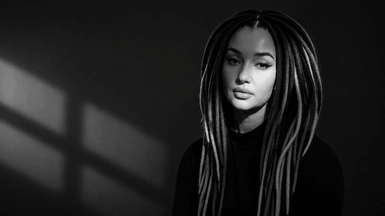 Black-and-white portrait of woman with long dreadlocks, soft lighting, calm expression against dark background