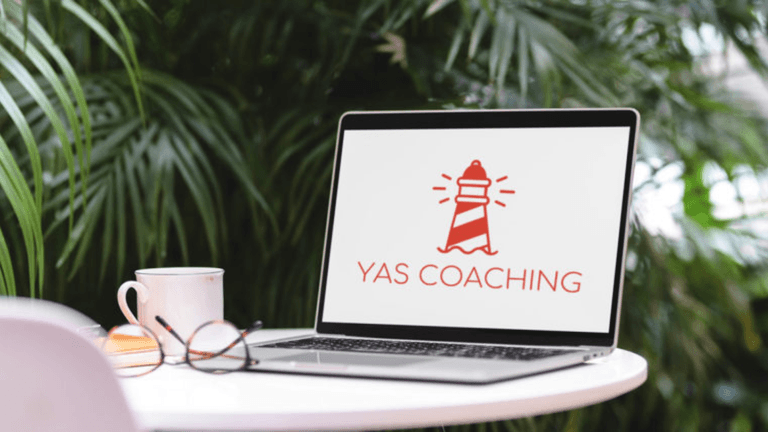 Laptop on outdoor table displaying YAS Coaching lighthouse logo beside coffee cup and glasses, symbolizing Yasmina Rauber’s leadership coaching work.