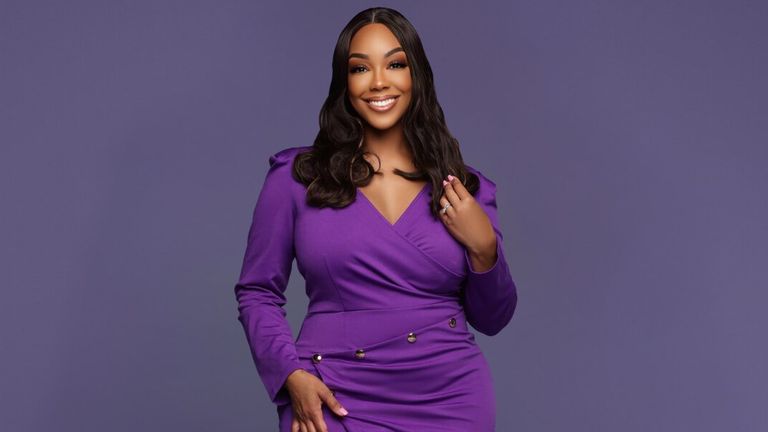 Portrait of Dr. Monica Moray smiling in a purple dress against a solid purple background.