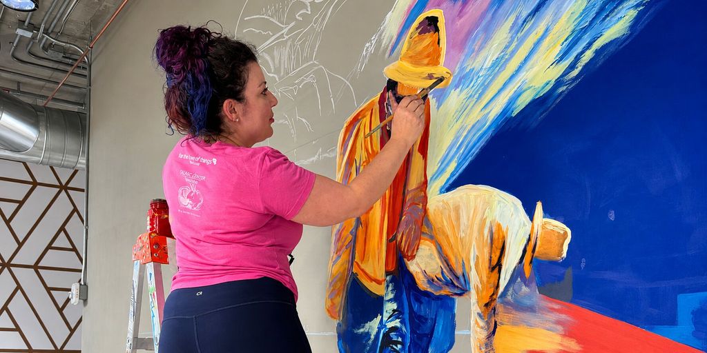 Hayley Ferreira painting a colorful custom mural on an interior wall.